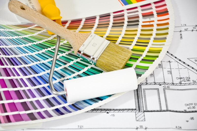 Un nuancier de couleurs vives avec un pinceau et un rouleau à peinture posés sur des plans d'architecte détaillés.
